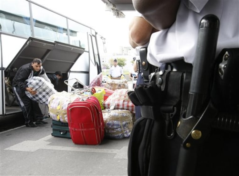 A police officer watches as Roma unload their luggage from a bus, before being expelled from France at Roissy airport, north of Paris, Thursday  Aug. 26 2010. The Archbishop of Paris, Andre Vingt-Trois has added to mounting criticism of the French government's crackdown on Gypsies, or Roma, calling it a \"circus.\" A poll says the French are split on the issue, and meanwhile the government puts more Roma on planes home to Eastern Europe. Citizens of Romania and Bulgaria, both EU member states, benefit from free circulation within the bloc, but the French labour market is not fully open to them and if they do not have a job and lodging after three months they are required to leave the country(AP Photo/Jacques Brinon)